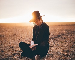 Person crouching in field holding book