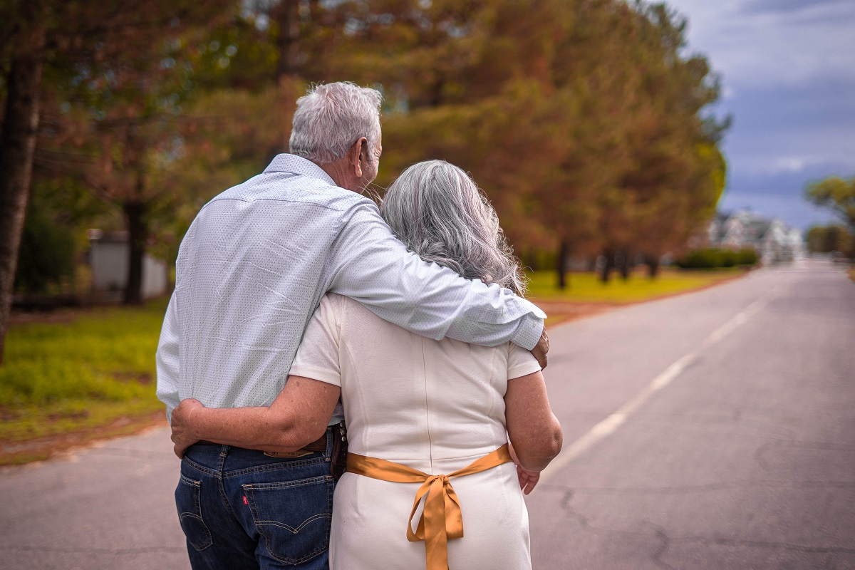 Couple in their 70s walking down road embracing one another