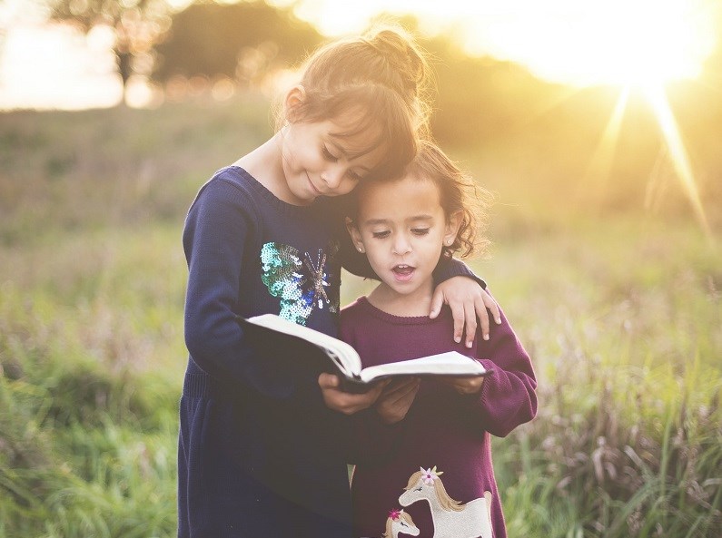 Two girls reading a book together outside