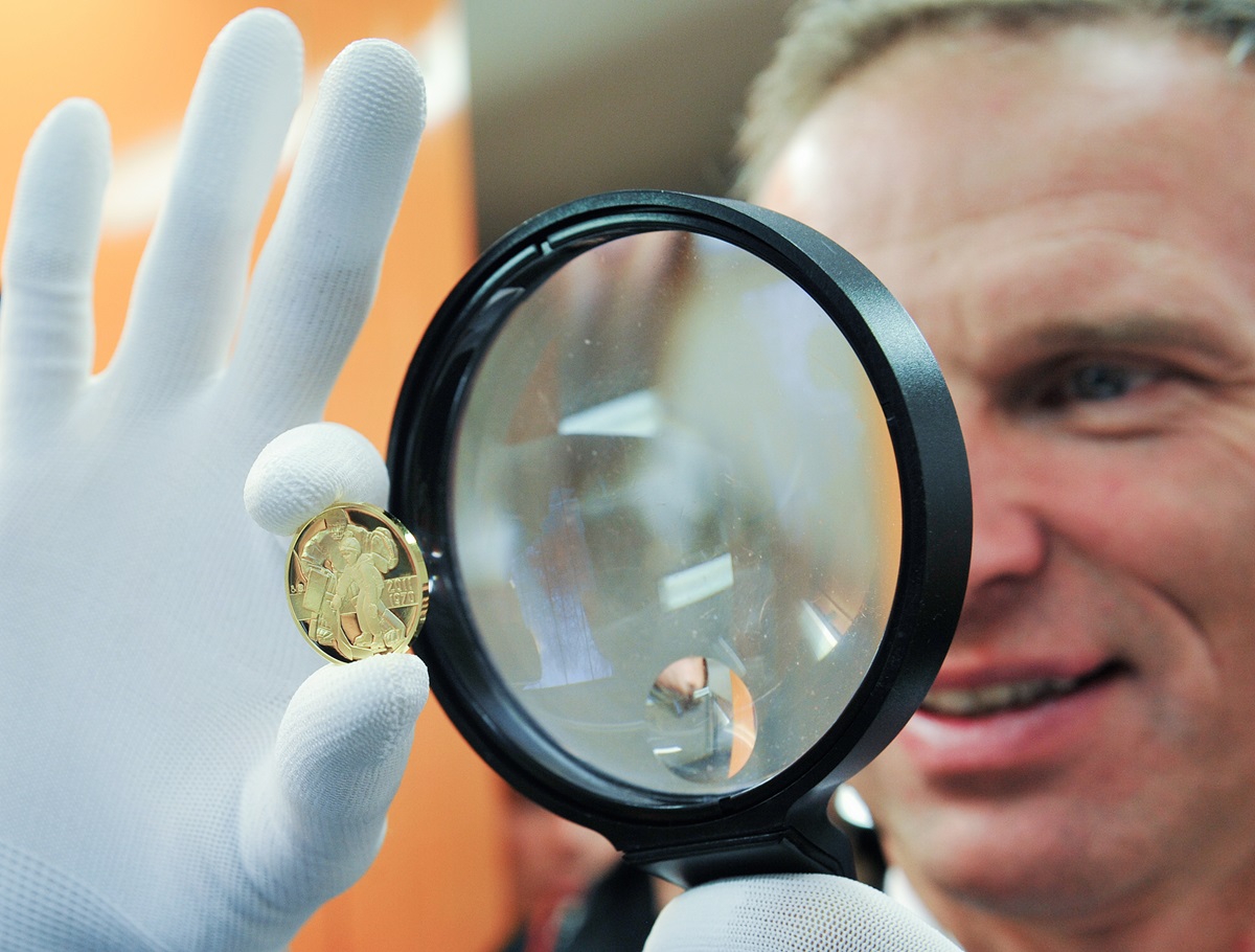 Man holding gold coin and looking through magnifying glass