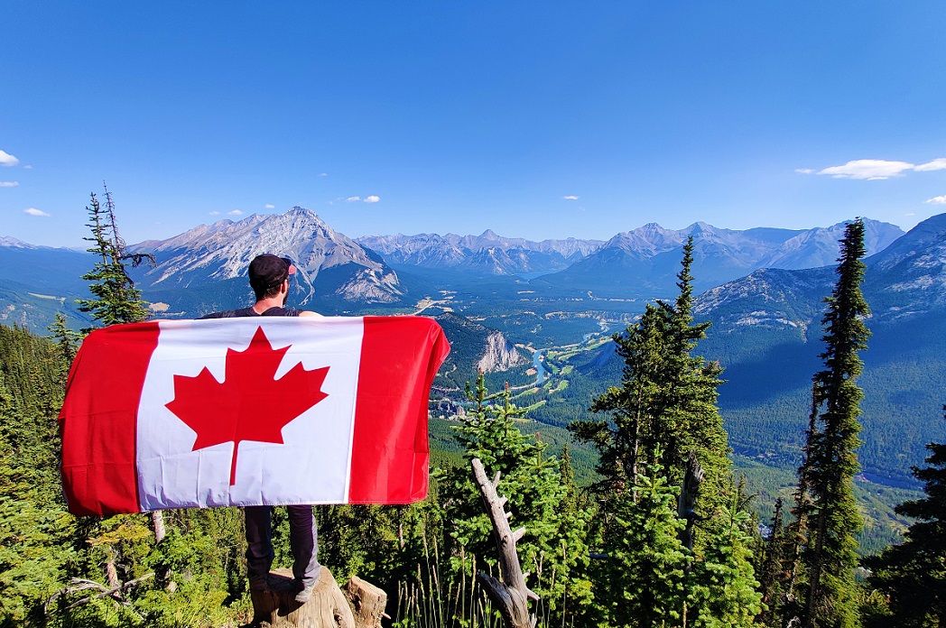 Person holding Canadian flag and standing over mountain range