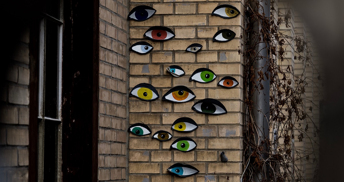 Installation artistique représentant des yeux de différentes couleurs sur un mur de briques.