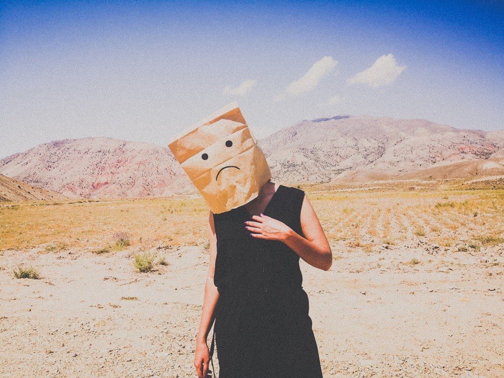 Person wearing a paper bag over their head with a sad face on it